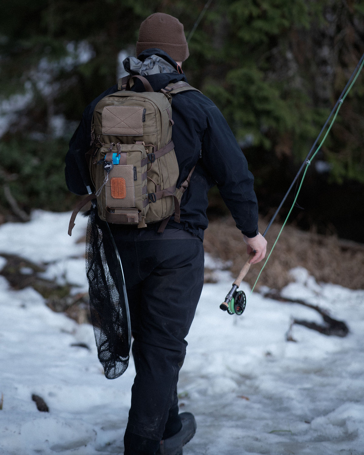 Person with a Savotta Rintamus attached to a Savotta Niukka backpack and fishing gear walking through a snowy forest