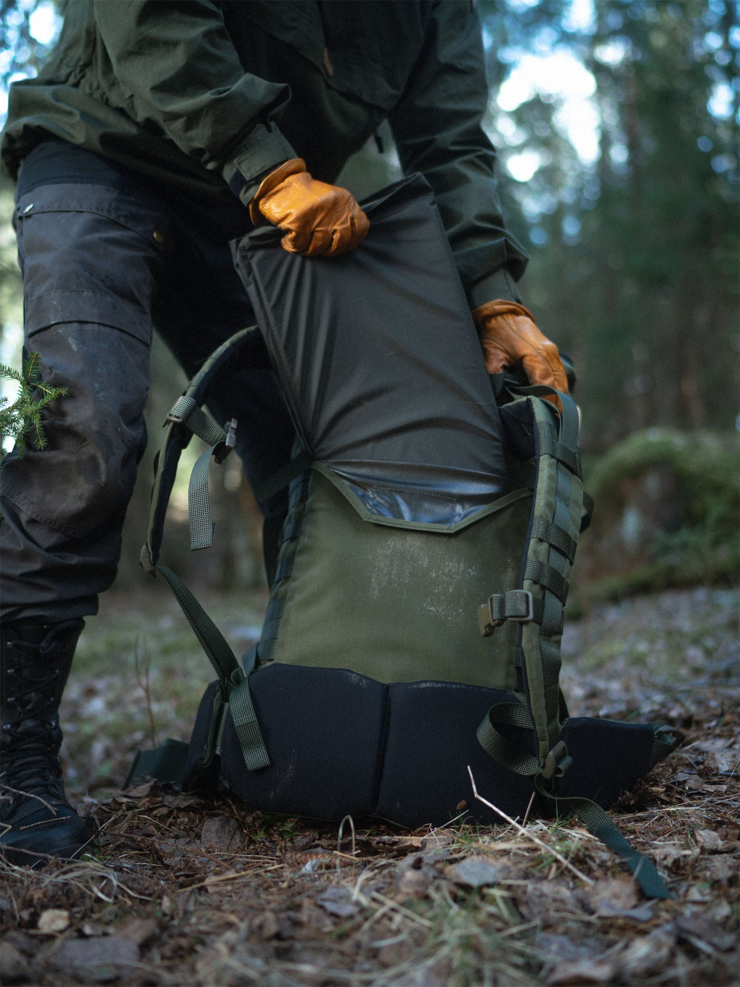 Person inserting Savotta sitting pad into Kantamus 40L backpack back panel in a forest setting