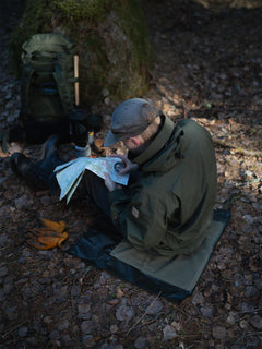 Person in a forest setting, sitting on Savotta sitting pad with a map and compass.
