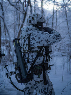 Person in camouflage gear wearing Savotta Varjelus Plate Carrier in a snowy forest.