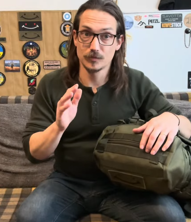 Man with glasses and long hair holding a Savotta backpack and sitting on a sofa