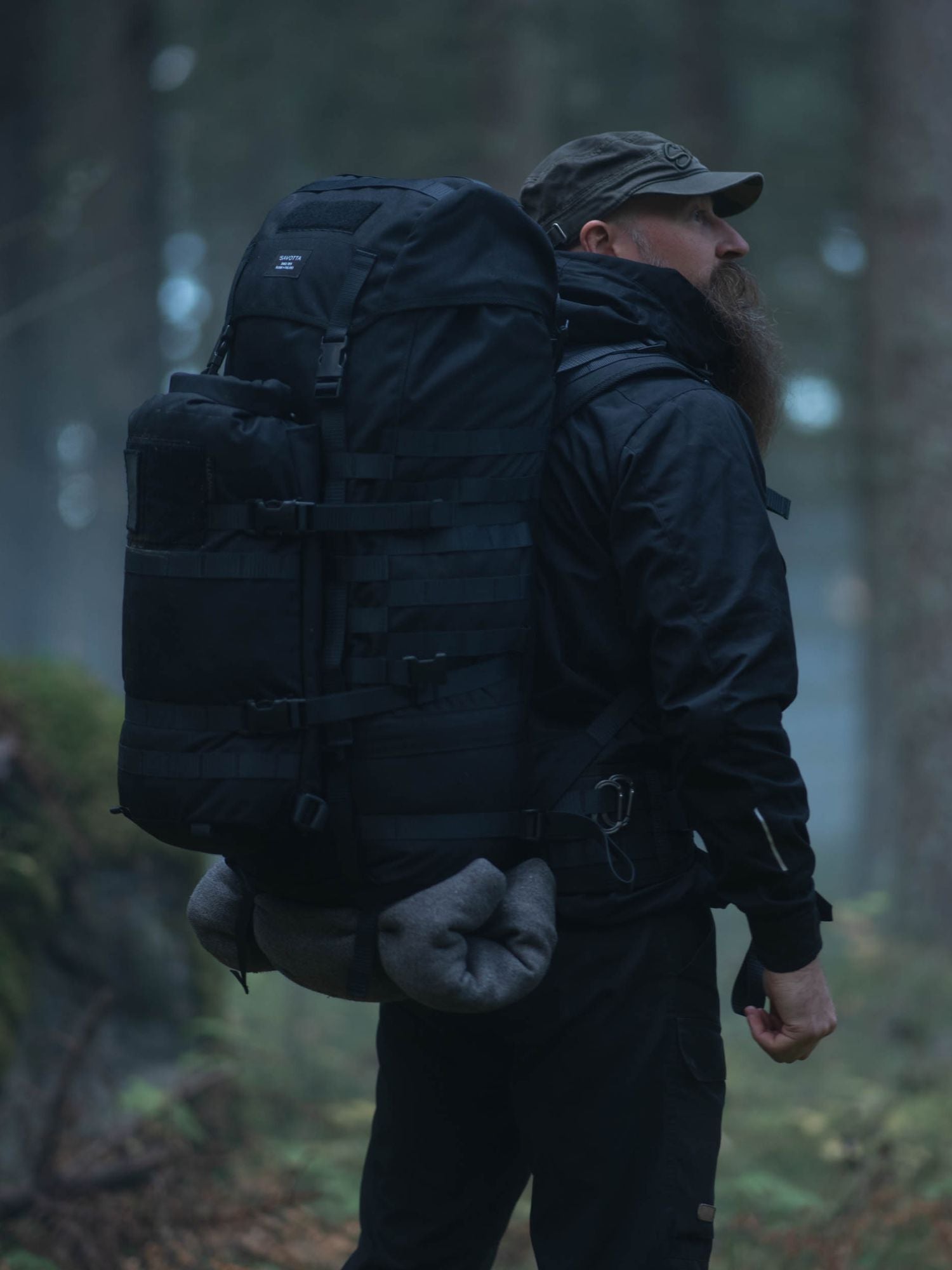 Person with a black Savotta Jääkäri backpack with a Savotta Hatka attached walking through a forest