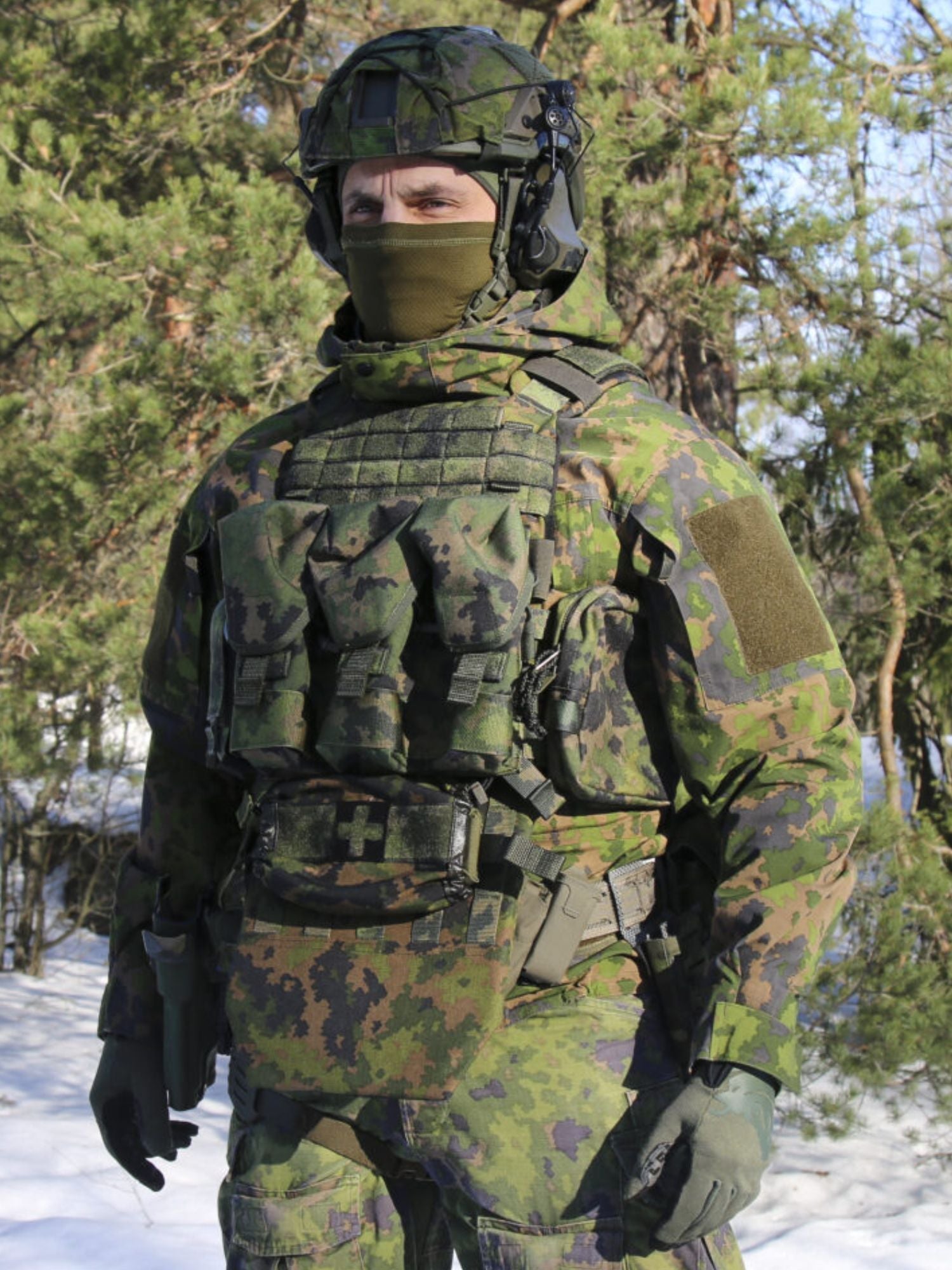 Person in camouflage military uniform with helmet and a Savotta Varjelus plate carrier standing in a snowy forest.