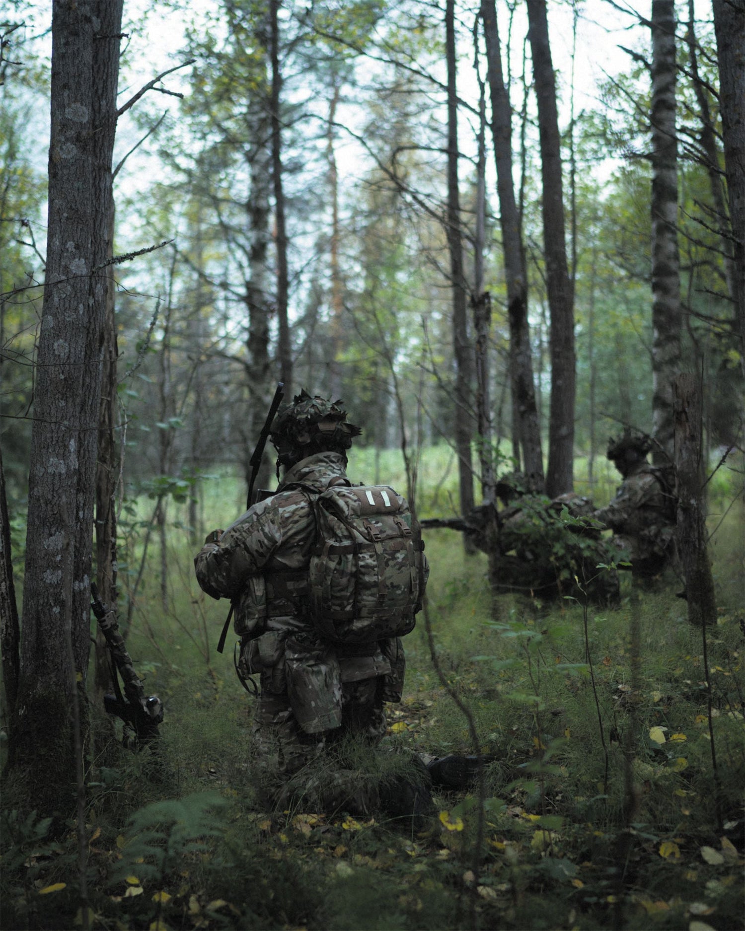 Three soldiers in camouflage gear walking through a forest.